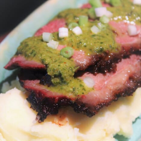 Sliced picanha is drizzled with chimichurri sauce ready to eat.