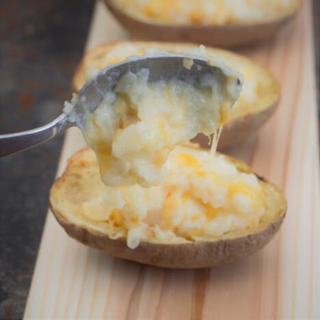 Potato skins having their filling scooped into them with a spoon.