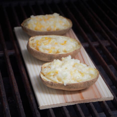 A plank with three stuffed potatoes sitting in a barbecue.