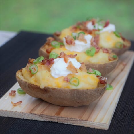 A BBQ plank with three garnished stuffed potatoes on it.