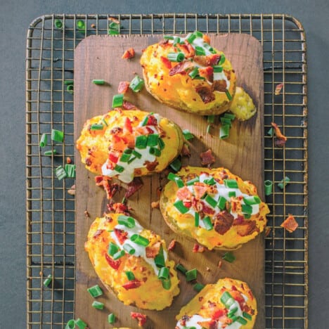 Looking down on stuffed potato skins sitting on a plank sitting on a cooling rack.