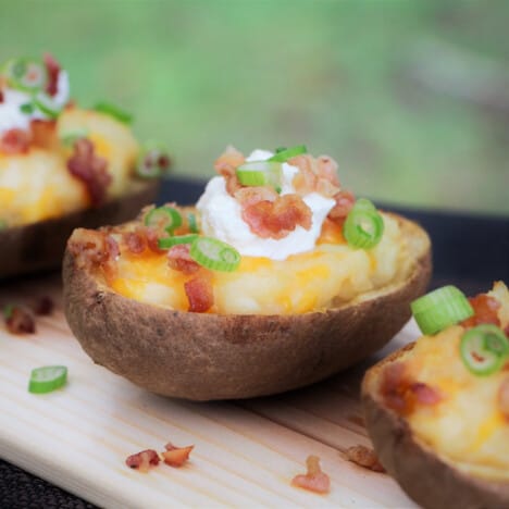 Cloe-up of a stuffed potato sitting on a plank garnished with sour cream, bacon and spring onions.