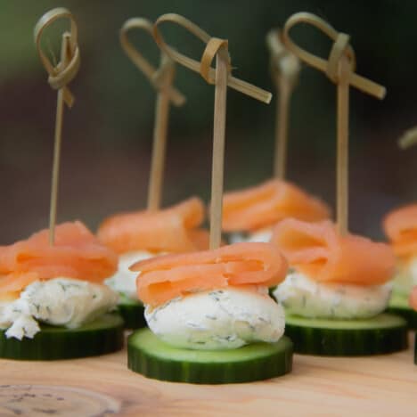 Smoked salmon cucumber bites are laid out on a platter waiting to be eaten.