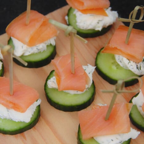 Looking down at smoked salmon cucumber bites on a wooden platter.