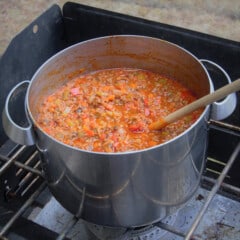 Spaghetti Bolognese simmering in a large pot on a gas stove.