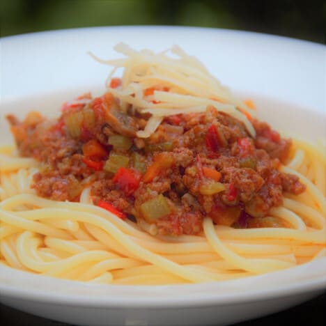 Spaghetti Bolognese served over pasta and topped with grated cheese in a shallow white dish.