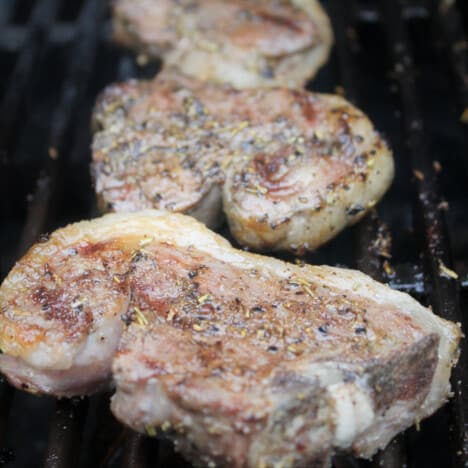 Three grilled and seasoned lamb chops lay on grill grates.