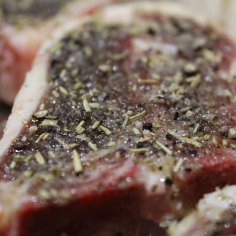 A close up of a single lamb chop with the dried rosemary seasoning on top.