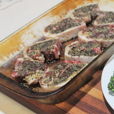 Marinated lamb chops sit in a glass baking dish waiting to be grilled.