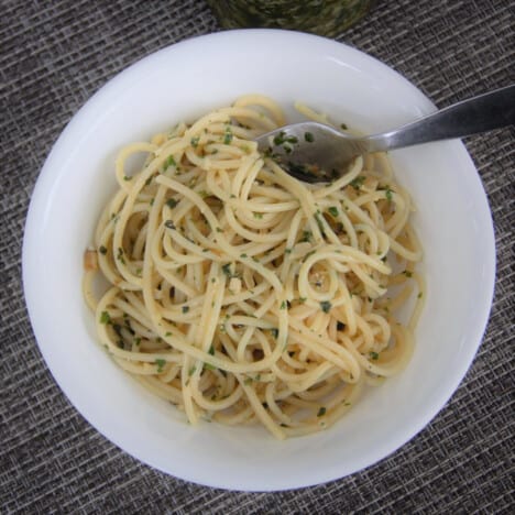 Ariel shot of cooked spaghetti noodles lightly tossed with walnut pesto in a white shallow bowl.