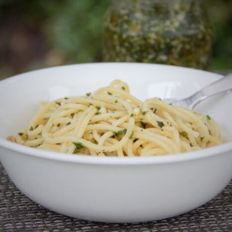 Looking at a white bowl holding cooked spaghetti tossed lightly with the walnut pesto.