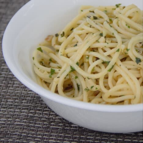 A white bowl holds cooked spaghetti noodles with a light topping of walnut pesto.