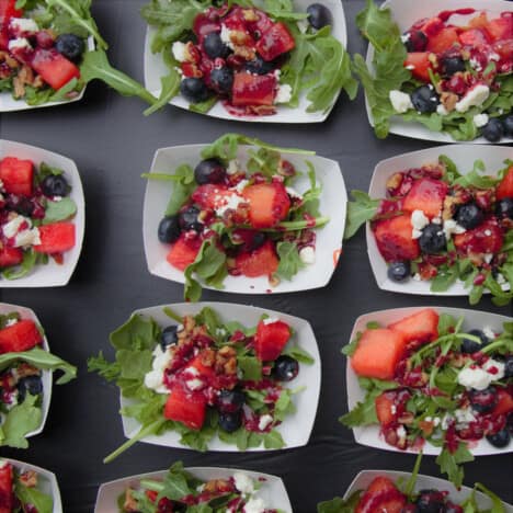 Individual portions of the watermelon and blueberry salad are served in small white paper boats.