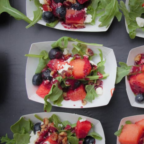 Small white paper bowls are lined up and filled with the watermelon and blueberry salad.