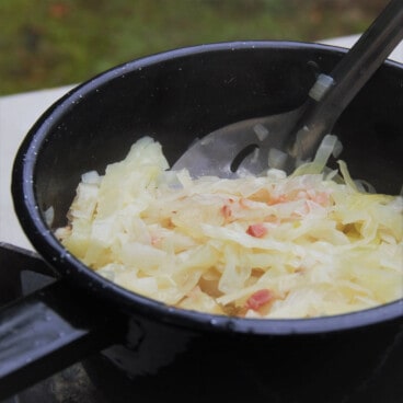 Bacon cabbage in a camp saucepan on a portable gas stove being stirred.