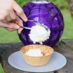 Ice cream being served from the novelty ice cream ball maker into a waffle cone cup.
