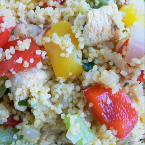 A plate full of red, yellow, and green bell peppers, cooked chicken, and couscous.