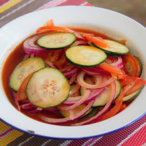 A bowl of sliced cucumbers, onions, and tomatoes marinates in the bloody Mary mix.