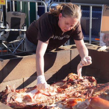 Saffron Hodgson taking meat from a whole hod srill sitting in a brick barbecue.