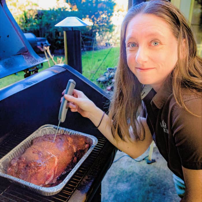 Saffron Hodgson looks at the camera while doing a temperature check on a smoked pork shoulder.