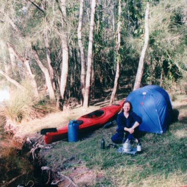 Safforn Hodgson Sitting in front of a kayak and hike tent cooking on a lightweight gas cooker