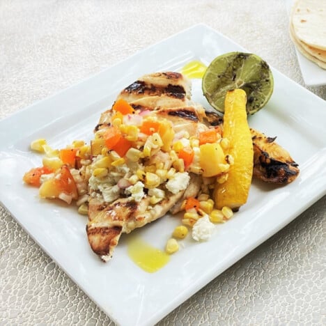 Plate of grilled chicken topped with a grilled corn and peach salsa.