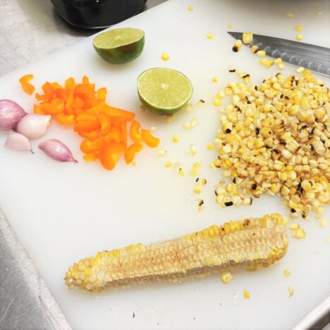 Chopping board with the corn and peach salsa ingredients in various stages of preparedness.