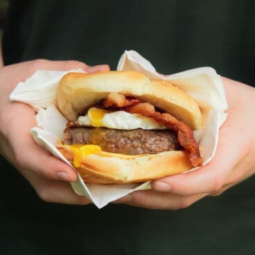 A Grilled Sausage Breakfast Burger being held in a napkin ready to eat.