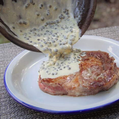 The creamy steak pepper sauce is being poured over a steak.