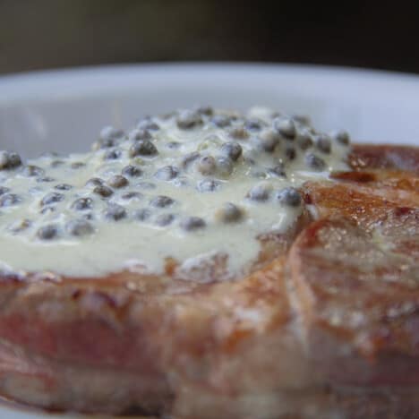 Close up photo of a rib eye steak topped with pepper sauce.