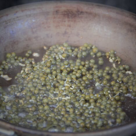 Green peppercorns, garlic, and white wine cooking in a small skillet.