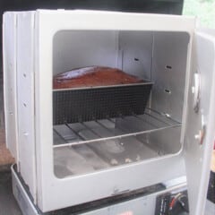 A flat-pack style camp oven sitting on a small gas stove cooking a cake