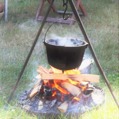 Dutch oven simmering over a campfire suspended on a tripod
