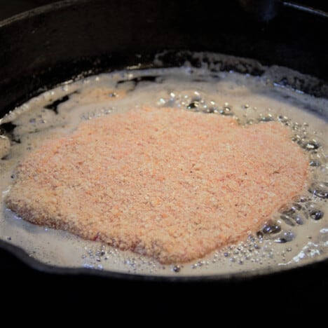 A fresh schnitzel is starting the cook in a skillet.