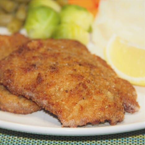 The schnitzel is served on a plate with vegetables and a wedge of lemon ready to be eaten.