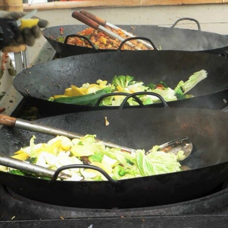Three woks with various stir fry dishes being cooked