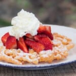 A plated funnel cake dusted with confectioner's sugar then topped with strawberries and cream.