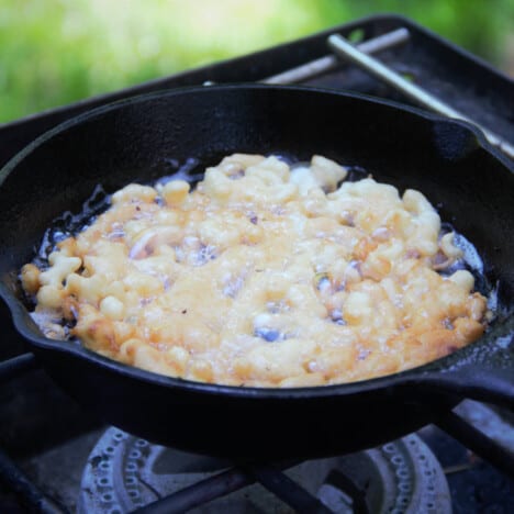 A funnel cake cooking in oil in a skillet almost ready for its turn to cook the other side.