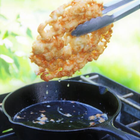 A golden brown funnel cake being removed from the oil in the skillet.