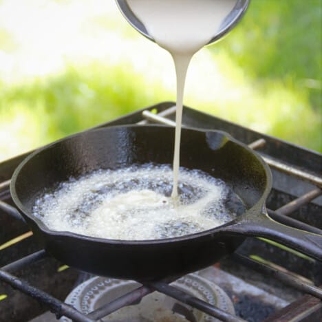 A stream of funnel cake batter being poured into hot oil in a skillet.
