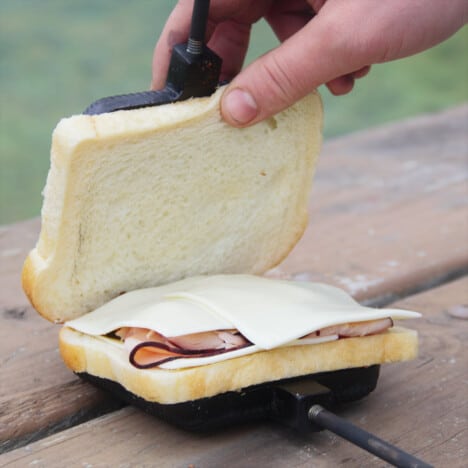 A ham and cheese sandwich being placed in the pie iron ready to be cooked.