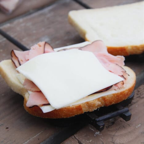 Cheese, ham, and bread sitting in a pie iron as it is being made ready to cook.