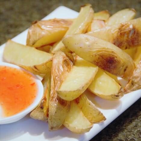 Barbecue potato wedges served with sweet chili sauce on a white platter.