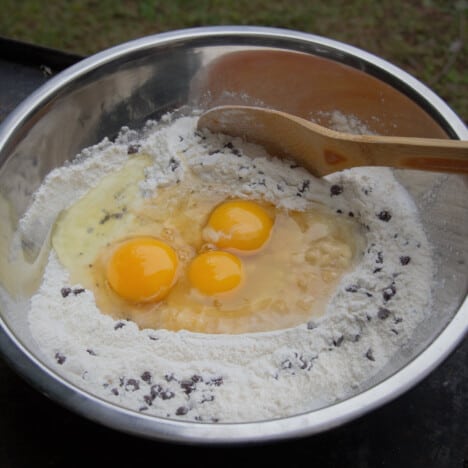 Stainless bowl with all the ingredients including three cracked eggs along with a wooden spoon.
