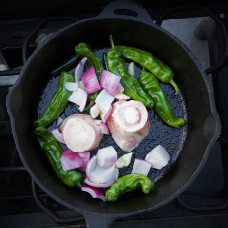 Looking down into a cast iron skillet with two rings of bone marrow, peppers, red onions, and garlic.