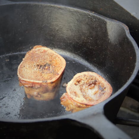 Two rings of bone marrow finish cooking in a cast iron skillet.