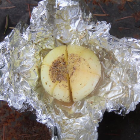 A cooked campfire foil onion sits in a crumpled piece of foil.