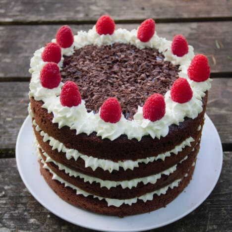 Looking down onto a finished chocolate raspberry cake with layers of cake and whipped cream, with fresh raspberries and shaved chocolate on top.