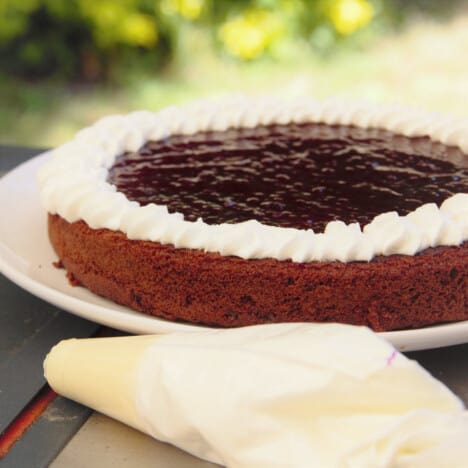 The first layer of chocolate cake sits on a plate, with a circle of piped whipped cream and raspberry jam.
