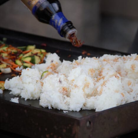 Soy sauce being added to white rice on a flat top griddle.